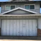 A two-story gray house with a large white garage door and red brick accents on a sunny day.